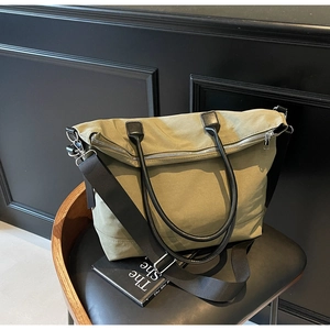 Détail du sac cabas en toile vert olive avec poignées en cuir noir posé sur une chaise