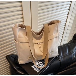 Detail of beige canvas tote bag featuring brown woven strap and BIDINO embroidery