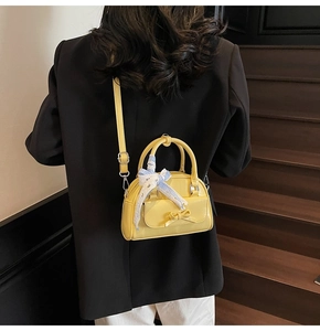 Rear view of a yellow mini Boston bag with ribbon detail on wooden stairs background