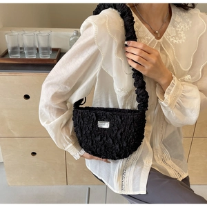 Detail of black pleated cloud bag with metallic nameplate and textured fabric handle