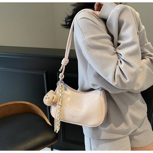Close-up of pink patent leather shoulder bag with decorative bow and plush bear charm