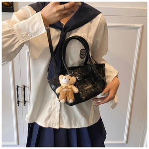 Detail of black woven leather handbag with a cute brown teddy bear plush charm