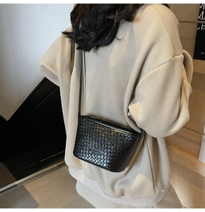 Détail du sac seau en cuir tressé noir porté par un mannequin dans un cadre minimaliste