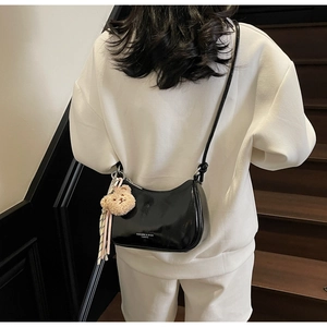 Detail of black patent leather half-moon bag with bear pendant worn by model on stairs