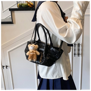 Detail of black woven tote bag with a cute brown teddy bear charm and adjustable strap