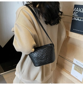 Détail d'un sac seau noir tissé porté avec un pull en maille côtelée beige et bandoulière