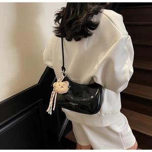 Detail of black patent leather half-moon shoulder bag with a cute brown teddy bear charm