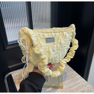 Detailed close-up of light yellow pleated handbag texture with metallic plaque