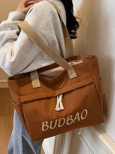 Brown canvas tote bag with wide beige shoulder straps and white knot decoration