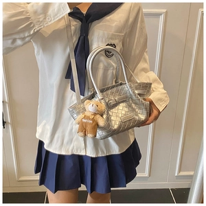 Detail of silver woven bucket bag with metallic texture and cute teddy bear charm accessory