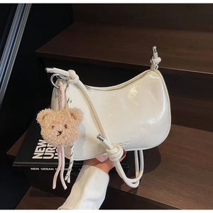 White patent leather shoulder bag with a cute plush bear charm on dark wood stairs