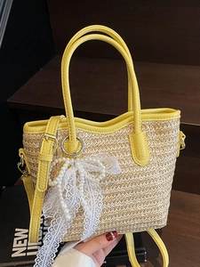 Woven straw bucket bag with yellow leather trim and pearl lace bow on wooden steps