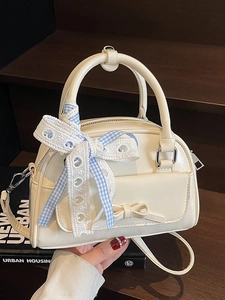 Cream white Boston handbag with bow pocket and lace ribbon shown on wooden stairs