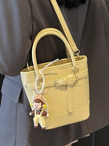 Pale yellow lychee texture bucket bag with cute doll charm and adjustable strap