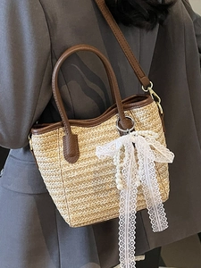 Contrast woven straw bucket bag with dark brown leather straps and pearl bow charm