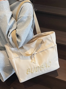 Large beige canvas tote bag with BUDBAO embroidery shown on a model on wooden stairs
