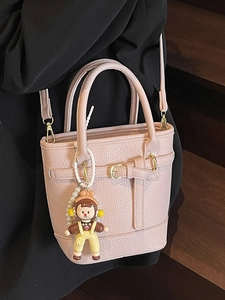 Pink lychee texture leather bucket bag with top handle and doll charm on black blazer