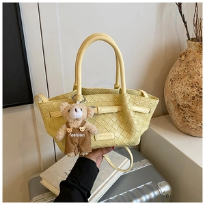 Detailed view of yellow woven basket bag with a cute teddy bear plush charm and logo