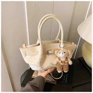 Detail of cream woven bucket bag featuring a cute teddy bear charm and leather strap