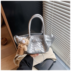 Detail of silver woven handbag with metallic texture and cute brown teddy bear charm