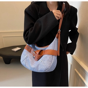 Détail du sac hobo en denim bleu clair avec lanières en cuir marron et boucles métalliques