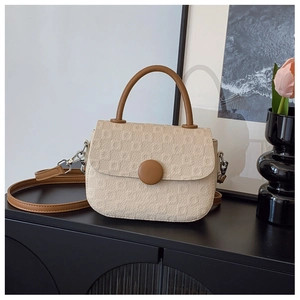 Detail of beige textured fabric handbag with brown leather strap and silver metal hooks