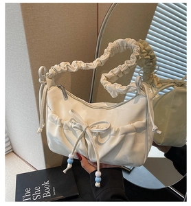 Detail view of white ruched shoulder bag with bow, blue beads and mirror reflection