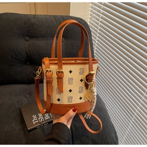 Detailed view of beige printed bucket bag with orange leather trim and tennis racket charm