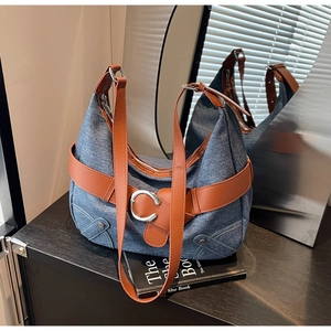 Détail d'un sac cabas en denim bleu avec lanières en cuir marron et boucles argentées