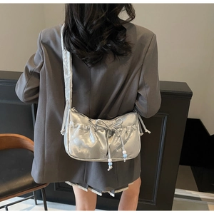 Detail view of silver pleated shoulder bag with bow and decorative beads on a model