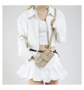 Detail of beige mini crossbody bag with litchi texture and gold metal buckle on model