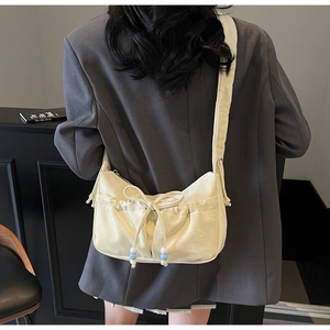 Detail of cream shoulder bag with bow tie, ruffles and blue beaded pendant on model