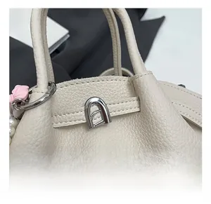 Macro detail of silver twist lock on beige lychee leather bag with pearl bow charm