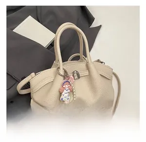 Close-up of beige pleated leather tote bag with cute doll charm and long shoulder strap