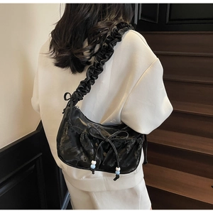 Detail of black pleated shoulder bag featuring bow straps and blue white beads