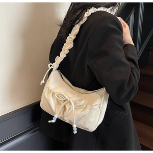Detail of cream pleated shoulder bag with oversized bow and beaded accents on strap
