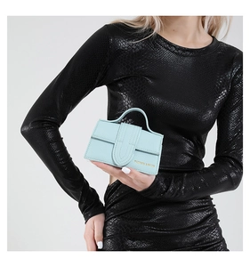 Detail of mint green mini square bag with leather texture held by a model in a dress