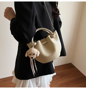 Sac seau à motif litchi avec pendentif chien montré dans un look bandoulière stylé