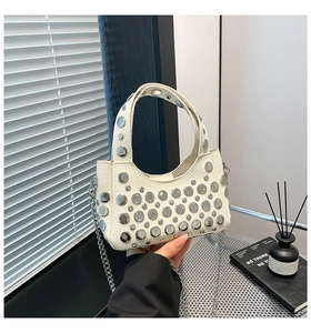 Dettaglio della borsa a secchiello in pelle bianca con rivetti metallici e catena