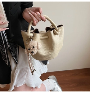 Détail du sac seau crème à motif litchi avec poignée nouée et charm de chien mignon