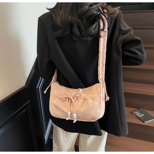 Detail of peach pink pleated shoulder bag with bow and beads on a wooden staircase