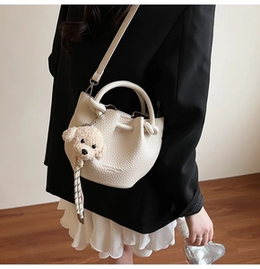 Détail du sac seau texturé litchi crème avec un pendentif en peluche petit chien