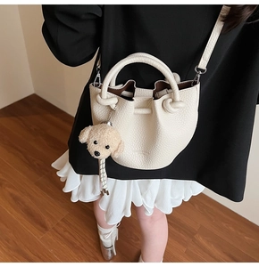 Gros plan du sac seau beige en cuir grainé avec poignée nouée et breloque chiot