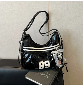 Gros plan du sac hobo en cuir verni noir avec écusson 89 blanc et breloque en dentelle