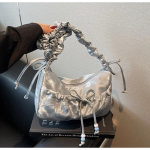 Detail of silver pleated cloud bag with bow ribbon and decorative beads on black prop