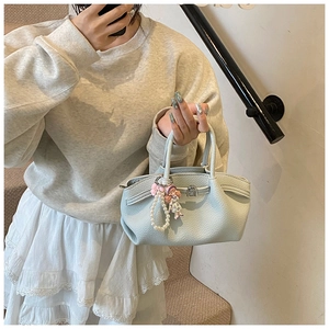 Detail view of light blue lychee pattern bucket bag with pearl and doll pendant on stairs
