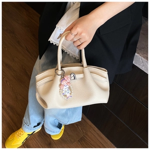 Detail of a creamy white pleated leather handbag featuring a cute pearl charm accessory