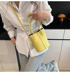 Detail of bright yellow pebbled leather bucket bag with top handle and crossbody strap
