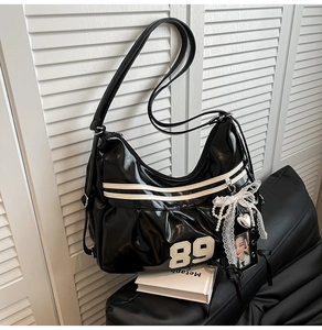 Détail du sac fourre-tout noir brillant avec écusson vintage et pendentifs style Y2K