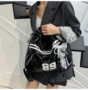 Détail du sac à bandoulière en cuir verni noir avec rayures blanches et nœud en dentelle